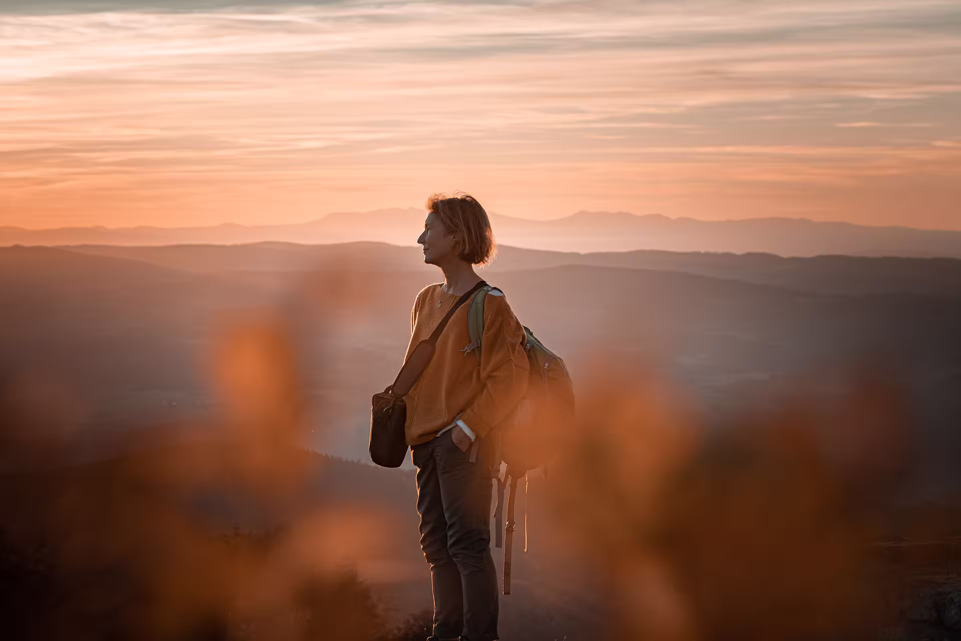 Femme avec sac à dos face aux montagnes au coucher du soleil